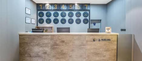 A reception desk with a clock display above it, a framed picture on the wall to the left, and a sign on the desk.
