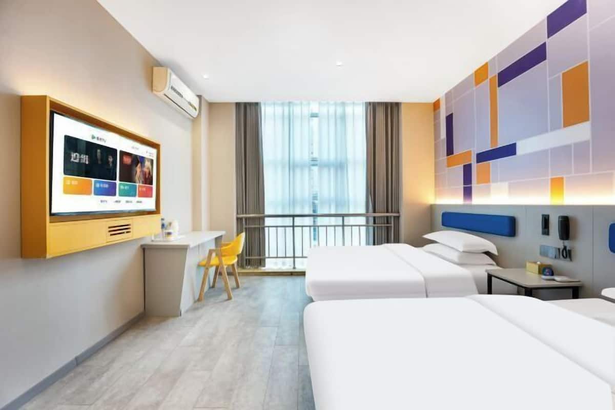 A hotel room with a bed, a desk, a chair, a TV, and a window with curtains.