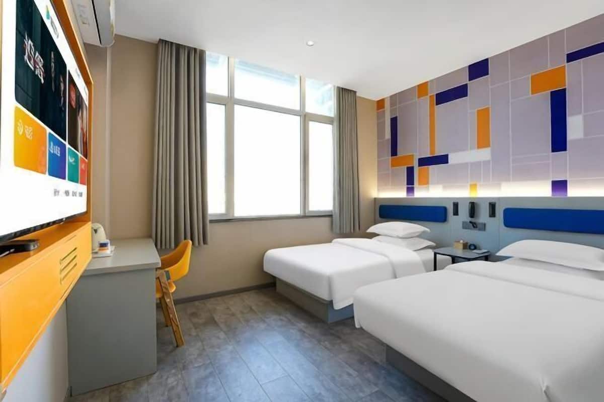 A hotel room with two beds, a desk, a TV, and a window with curtains.