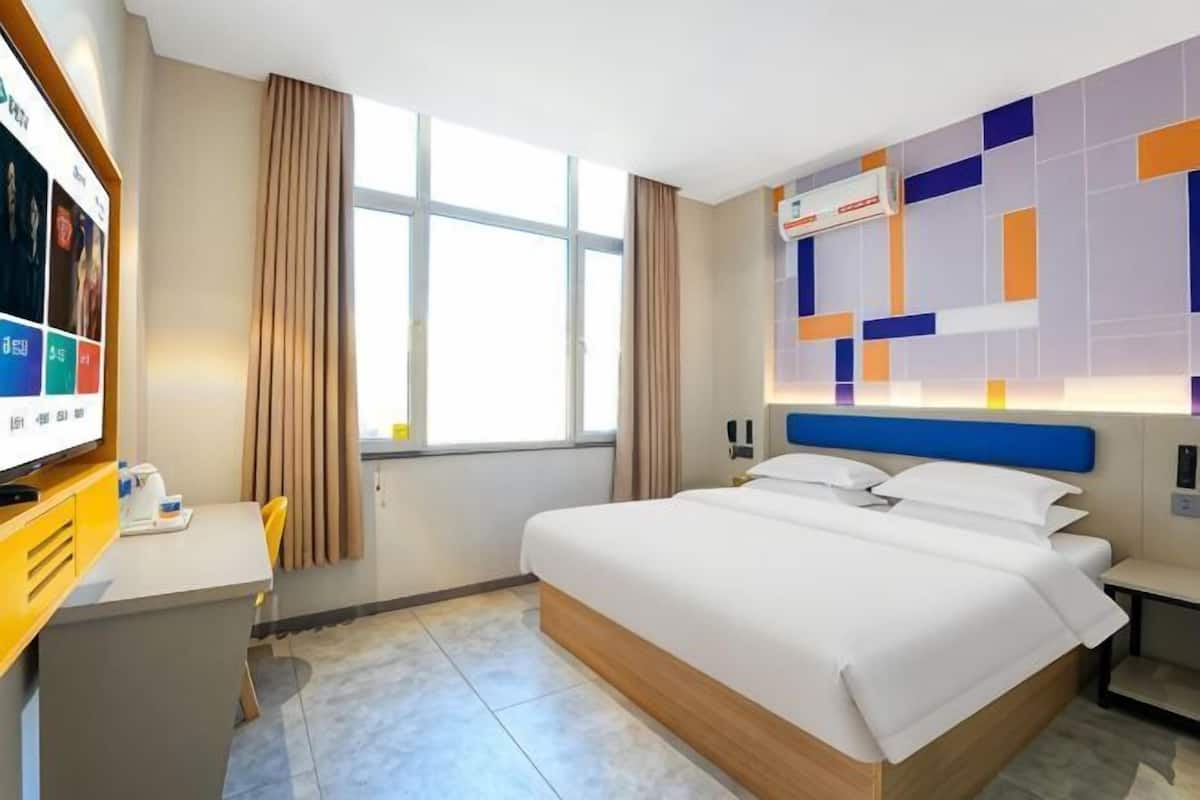 A hotel room with a bed, a desk, a TV, and a window with curtains.