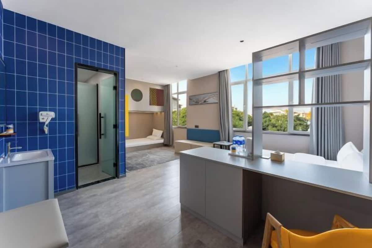 A modern hotel room with a kitchen area, a dining space, and a large window offering a view.