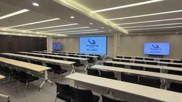 A conference room with rows of tables and chairs, a projector screen, and a presentation screen.