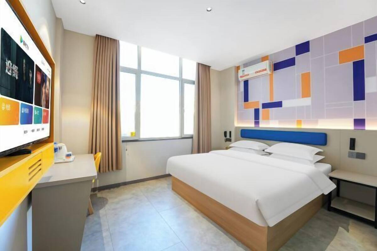 A hotel room with a large bed, a desk with a flat-screen TV, and a wall with a geometric pattern.