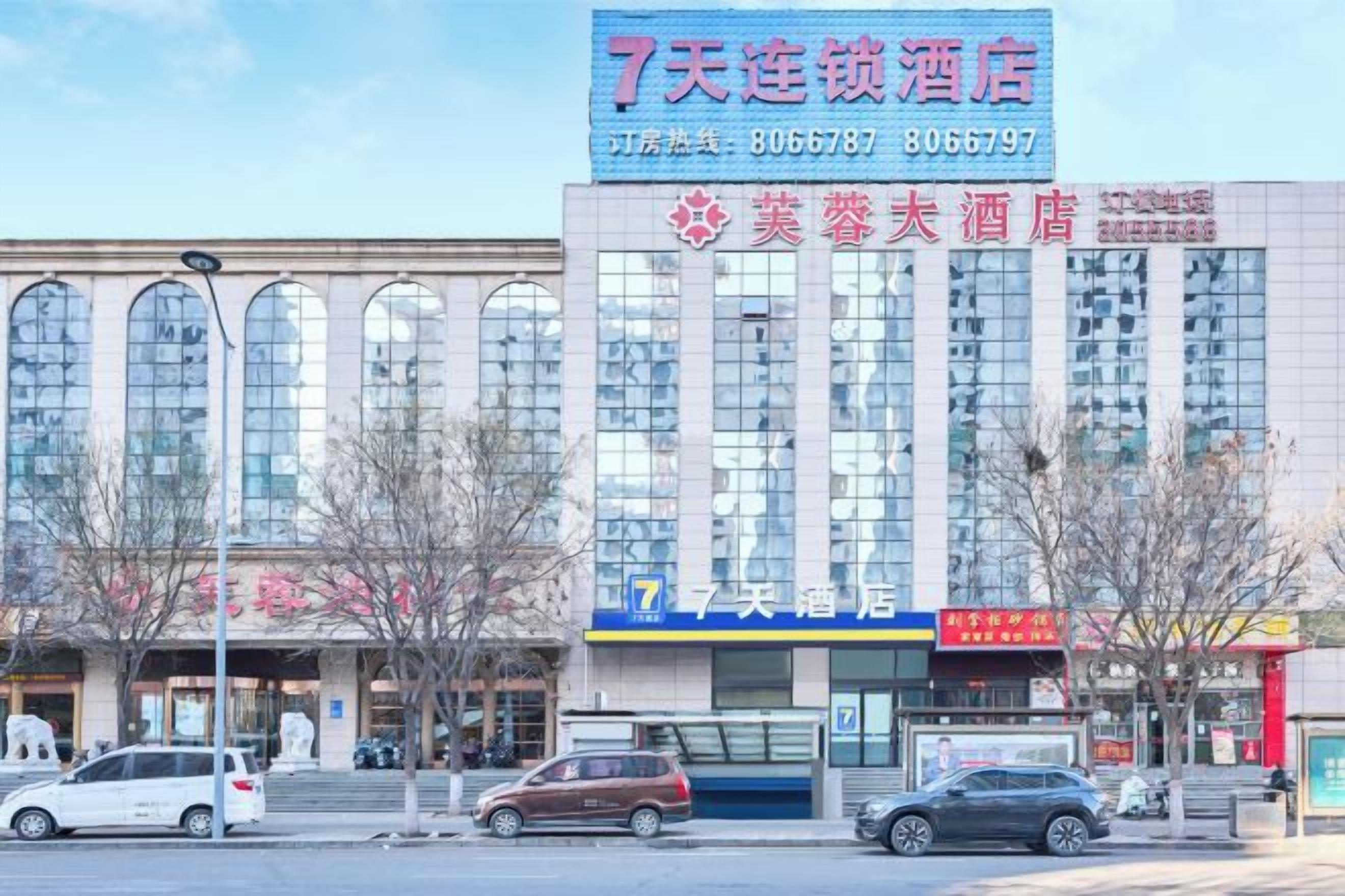 A hotel with a large sign, multiple windows, and a few parked cars in front.