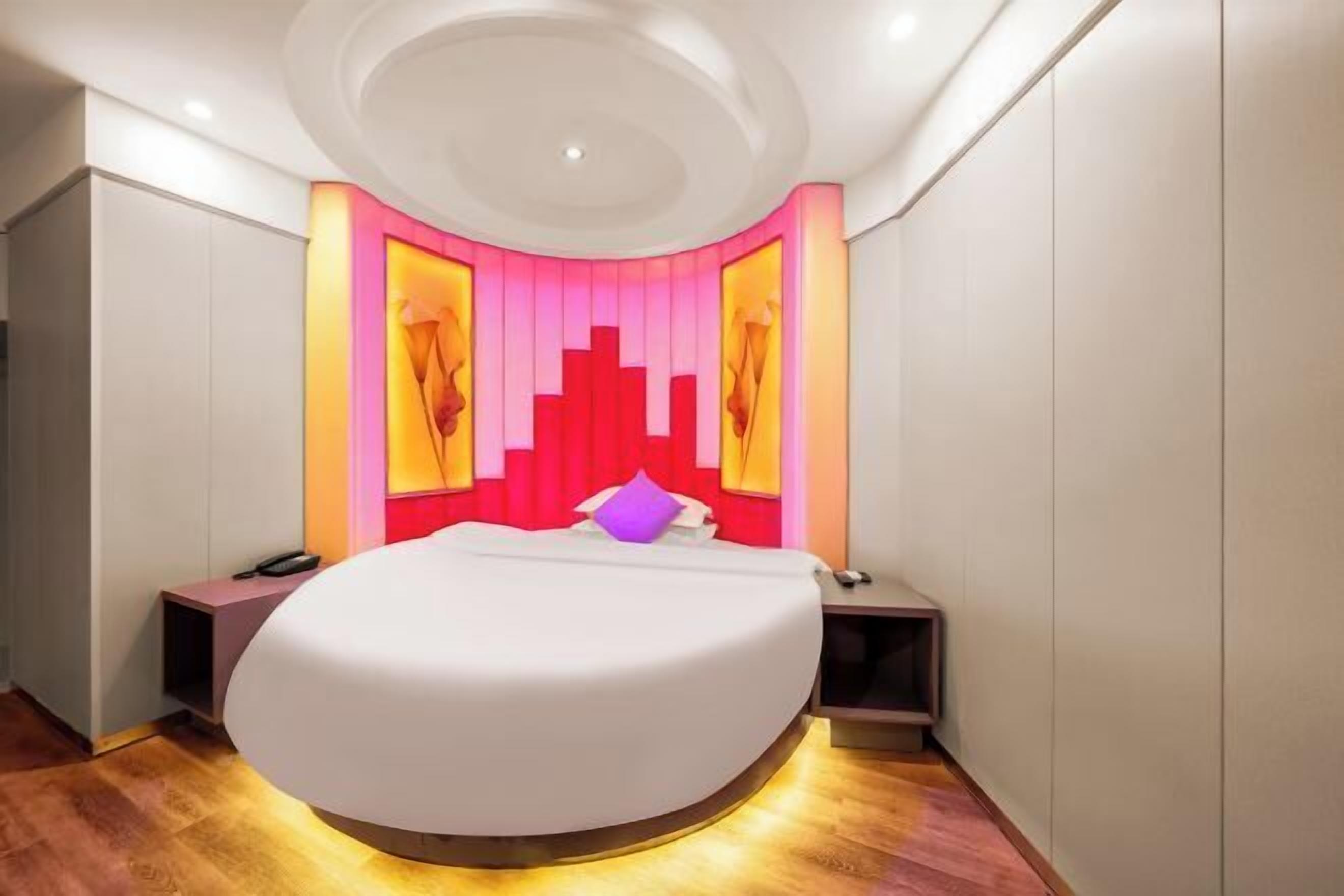 A modern bedroom with a large bed, a round ceiling light, and a pink accent wall.