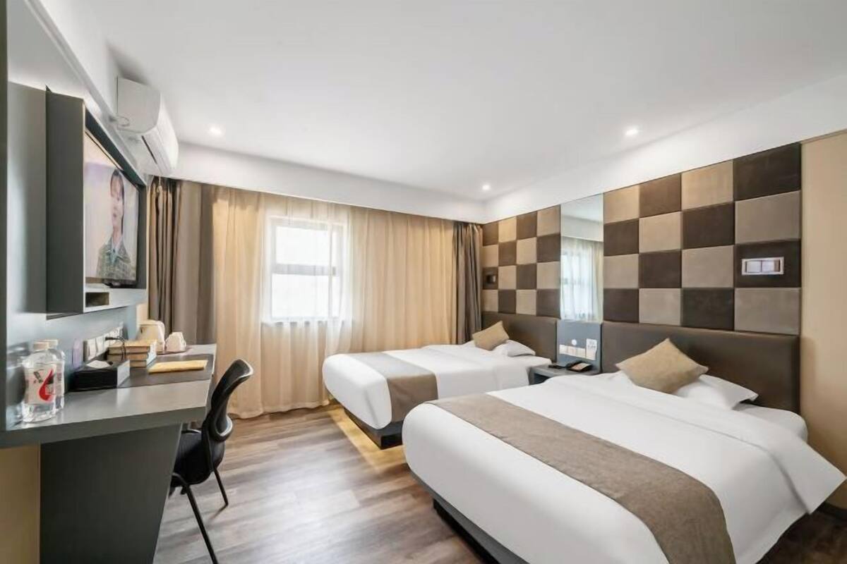 A hotel room with two beds, a desk, and a large window with curtains.