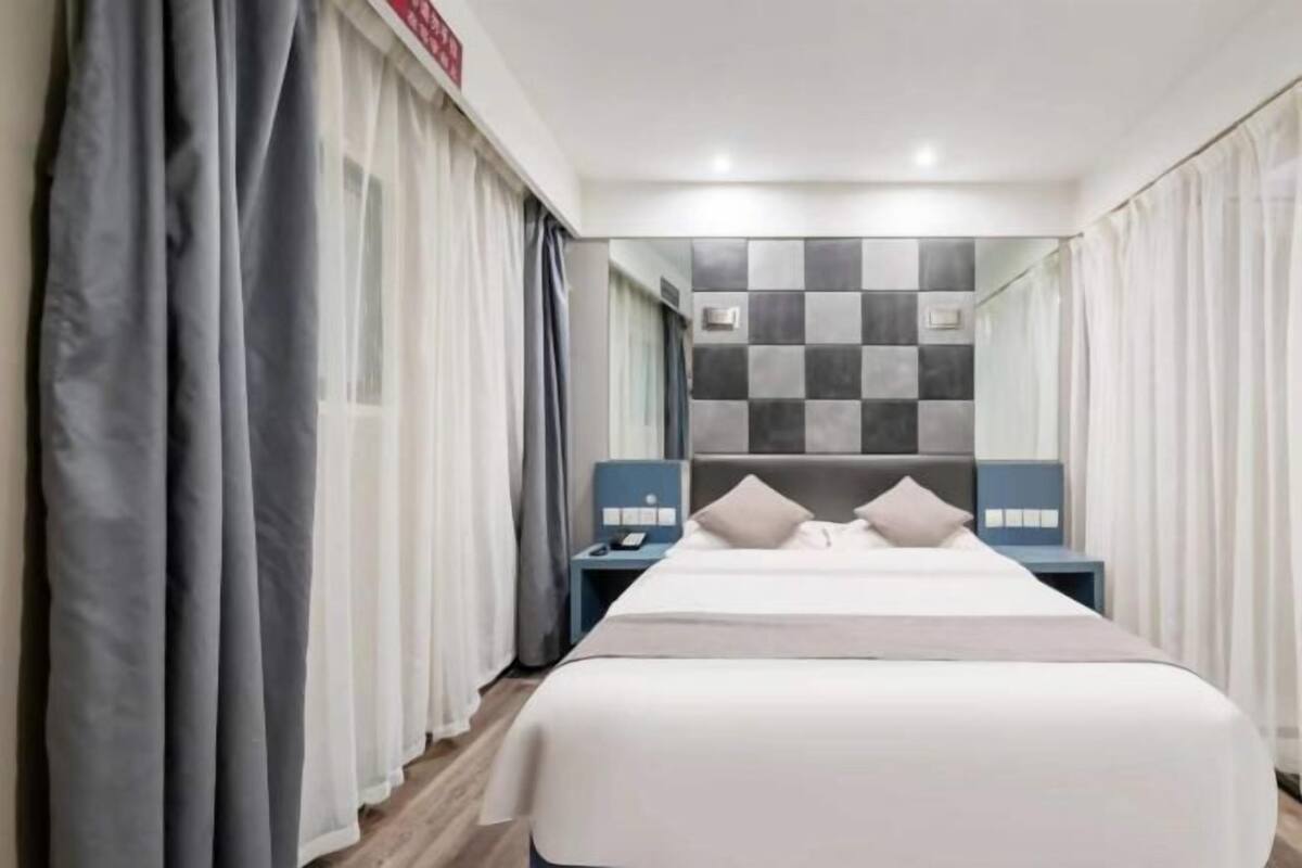 A hotel room with a large bed, a nightstand, and a mirror on the wall.