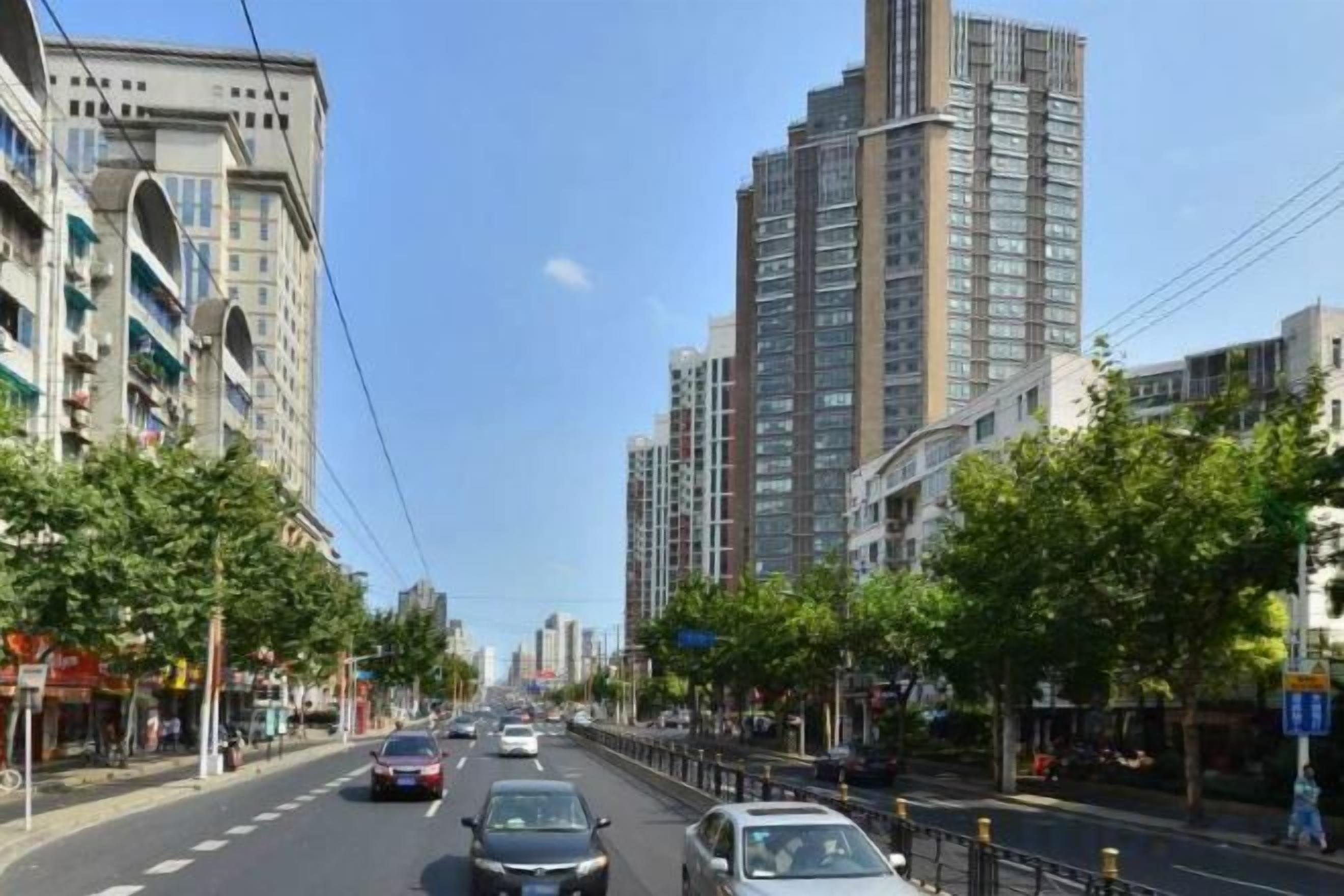 Uma rua urbana com edifícios altos, céu claro e carros na pista.