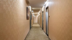 A long, narrow hotel corridor with doors on both sides, carpeted floors, and light-colored walls. - Sushi Select Hotel (Caoyang Road Subway Station) (Shanghai)