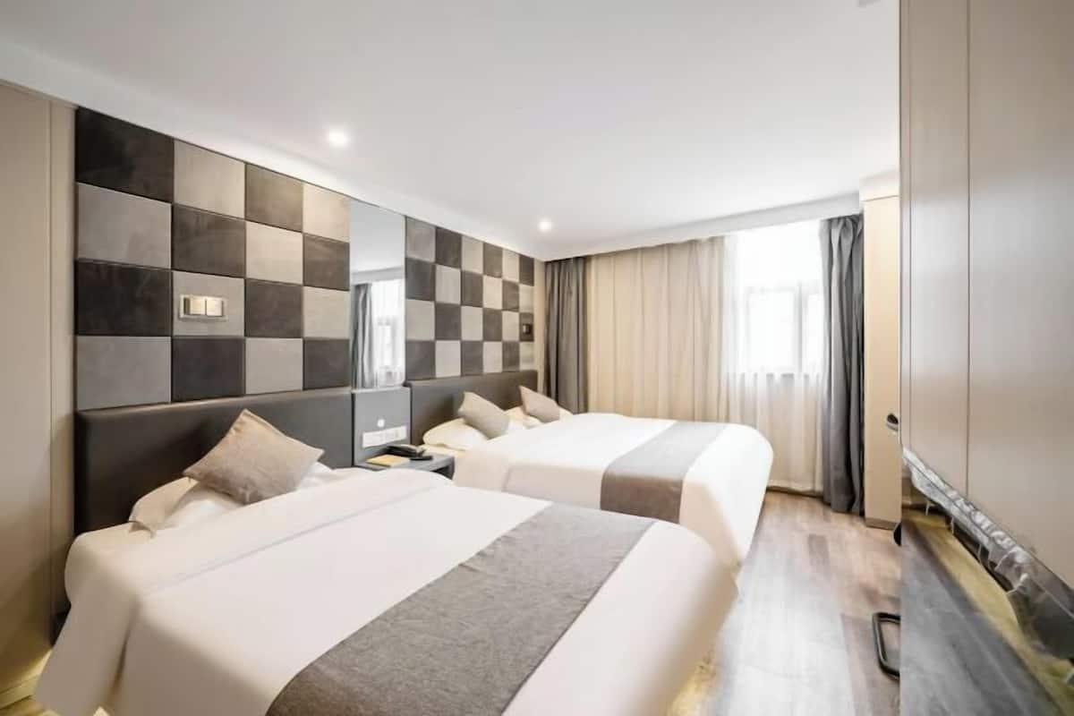 A hotel room with two beds, a modern checkered wall, a nightstand, and a large window with curtains.