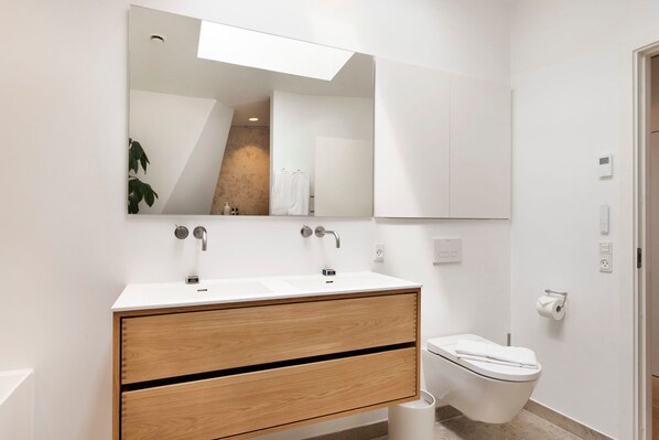 A modern bathroom with a white vanity, double sinks, and a toilet. - Dinesen Collection Signature Penthouse by Royal Theatre (Copenhagen)