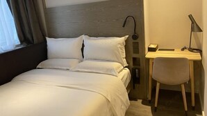 Una habitación de hotel con cama, escritorio, silla, lámpara y ventana con cortinas.