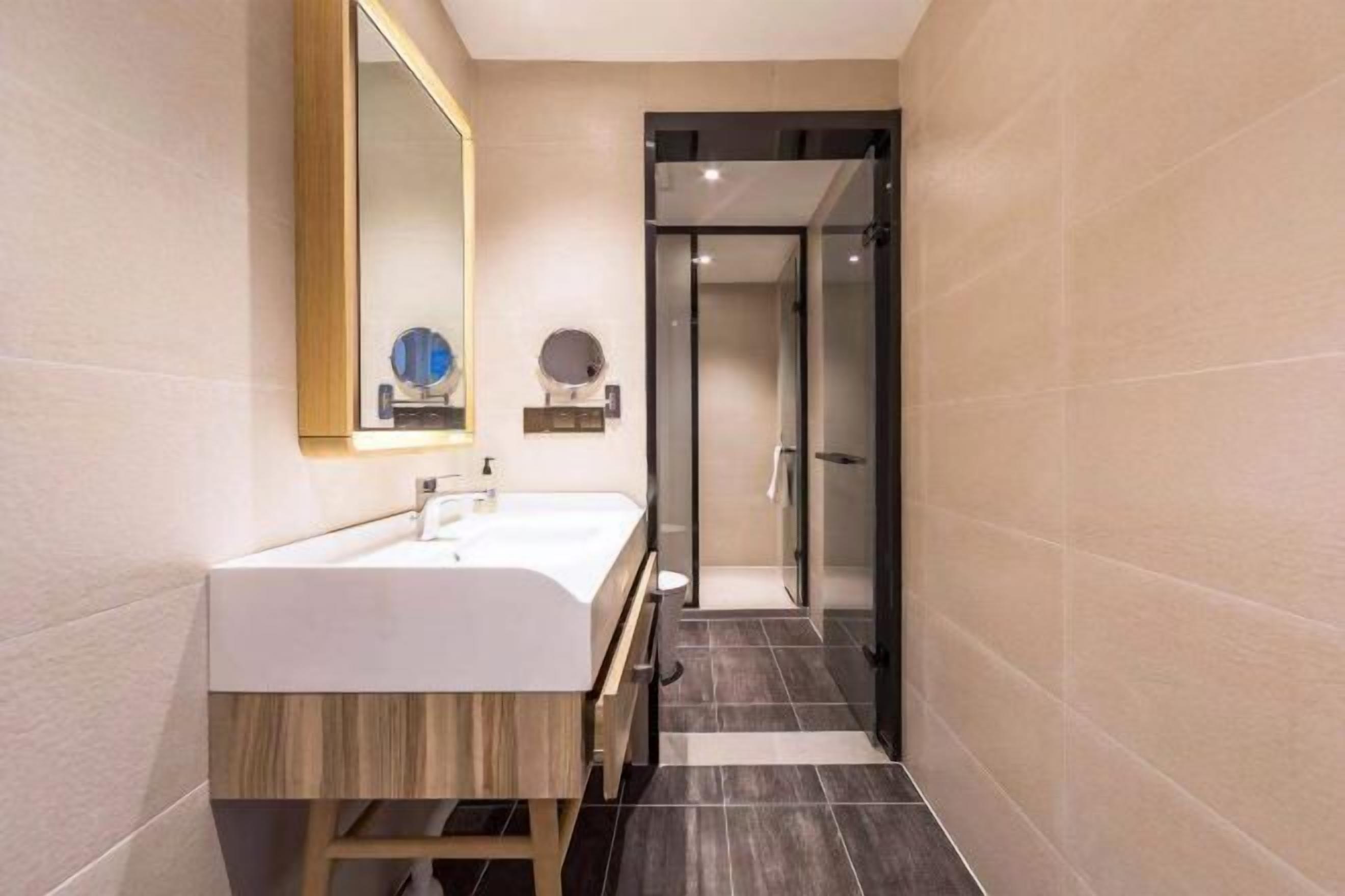 Un baño moderno con tocador de madera, un espejo grande y mampara de vidrio.