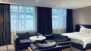 Una habitación de hotel con cama, sofá, una mesita y amplias ventanas con cortinas.