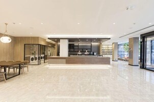 Un vestíbulo amplio con una recepción, zona de estar y una cocina moderna al fondo.