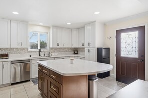 A modern kitchen with white cabinets, a large island, stainless steel appliances, and a window.