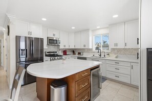 A modern kitchen with white cabinetry, stainless steel appliances, and a central island. - 4-bedroom house in beautiful Huntington Beach with WiFi, AC. (Huntington Beach)