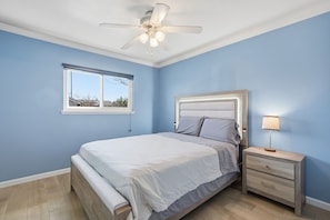 A bedroom with a bed, a nightstand, a lamp, a ceiling fan, and a window. - 4-bedroom house in beautiful Huntington Beach with WiFi, AC. (Huntington Beach)