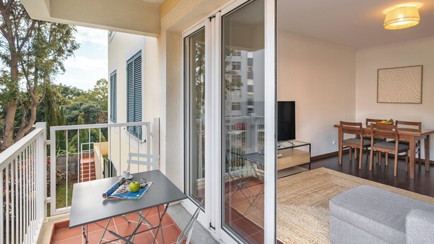 Un balcon avec une table et des chaises, un canapé et un téléviseur, dans un appartement moderne.