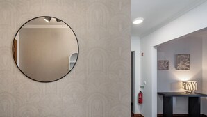 Un couloir avec un grand miroir rond au mur, un extincteur et une table avec une lampe.