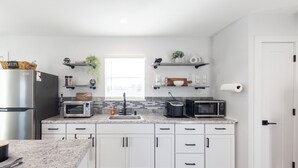 Eine moderne Küche mit weißen Schränken, einer Granit Arbeitsplatte, einem Edelstahlkühlschrank, einem Toaster, einer Mikrowelle und einem Spülbecken.