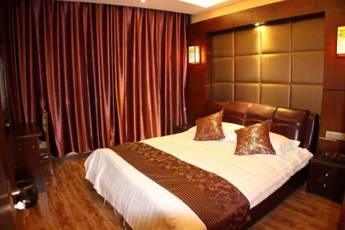Ett hotellrum med en stor säng, ett mörkt träfärgat sänggavel och en bakgrund av draperier.