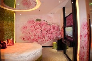 Ett hotellrum med en säng, en väggmålning med rosa rosor, en tv och en spegel.