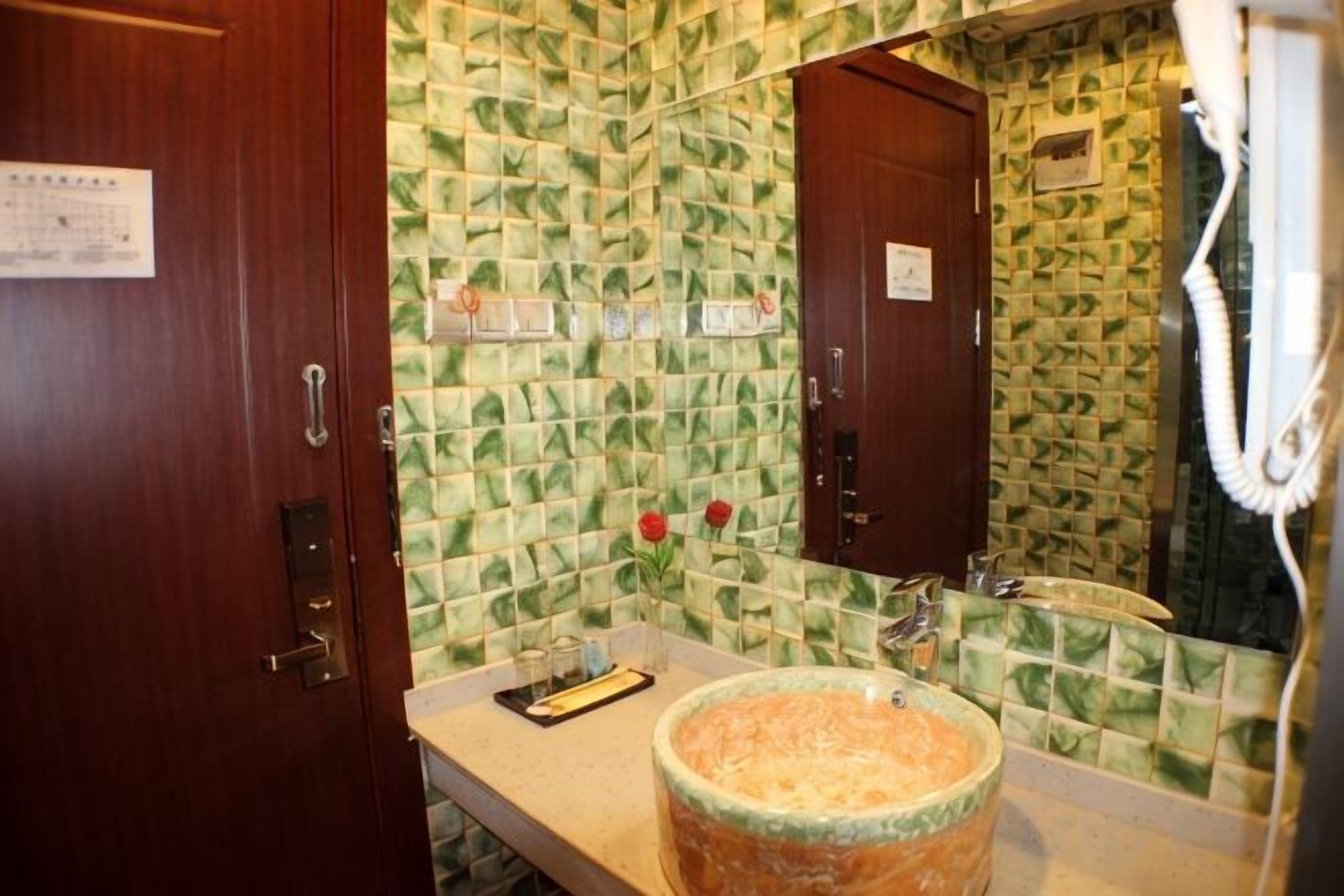 Un baño con pared de azulejos, puerta de madera, lavamanos con recipiente grande y espejo.
