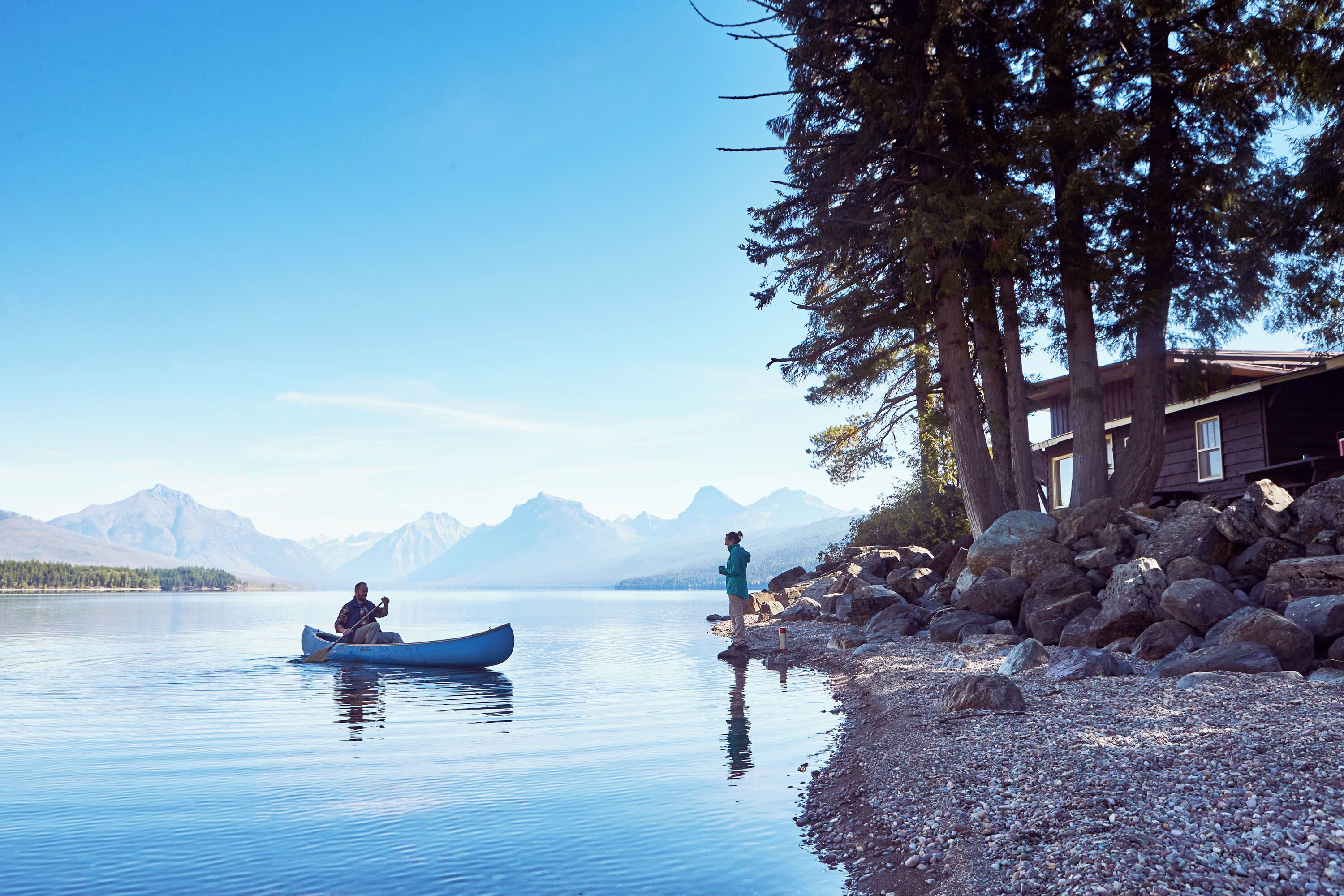 A calm lake with a wooden cabin and a rocky shoreline.