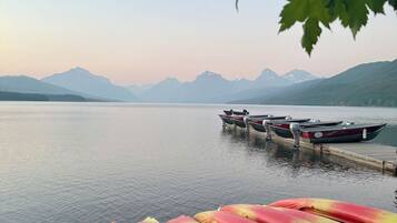 A row of colorful kayaks lined up at a dock with a calm lake and mountains in the background.
