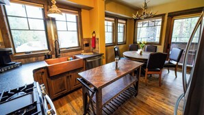 A kitchen with wooden cabinets, a central island, and a dining area with a table and chairs. - Apgar Lookout Suites (West Glacier)
