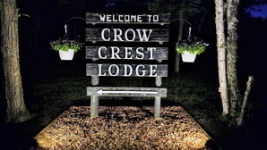 Une enseigne en bois portant l’inscription « BIENVENUE AU GROW CREST LODGE » et deux pots de fleurs suspendus.