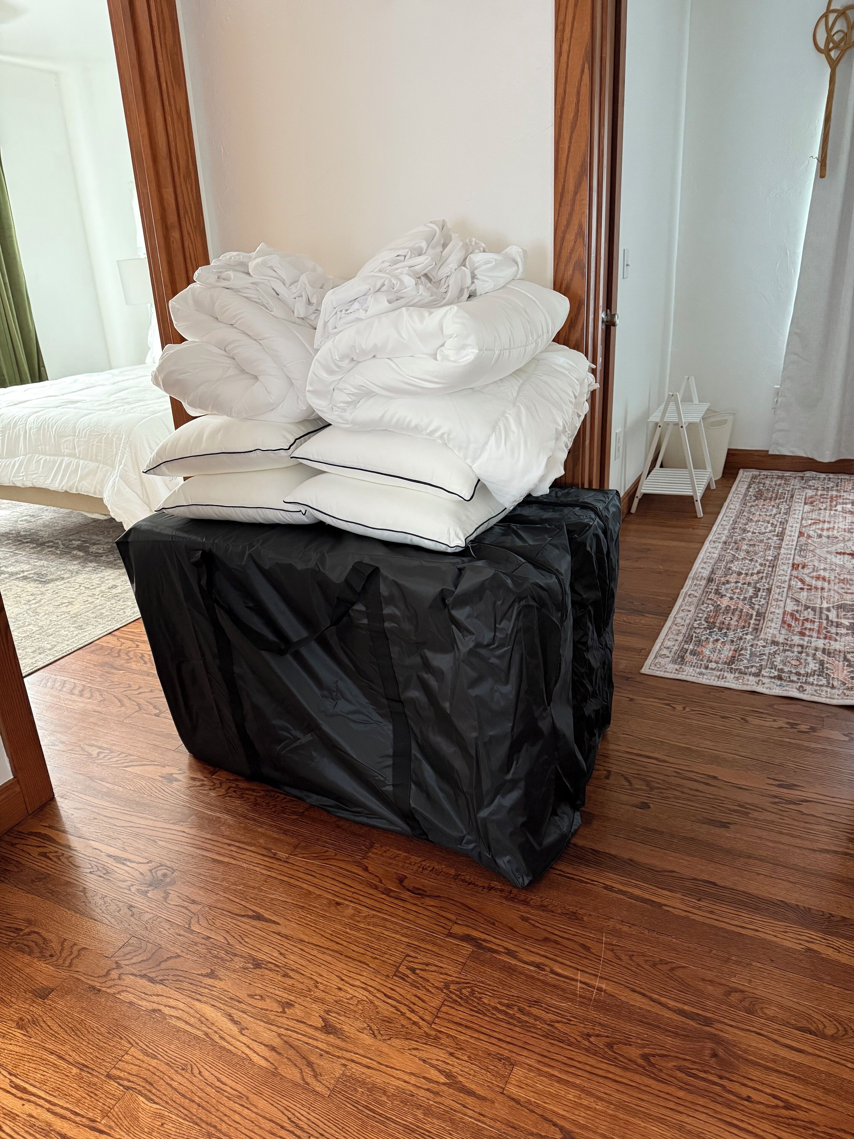 A neatly made bed with white bedding and a black cover on a wooden floor.