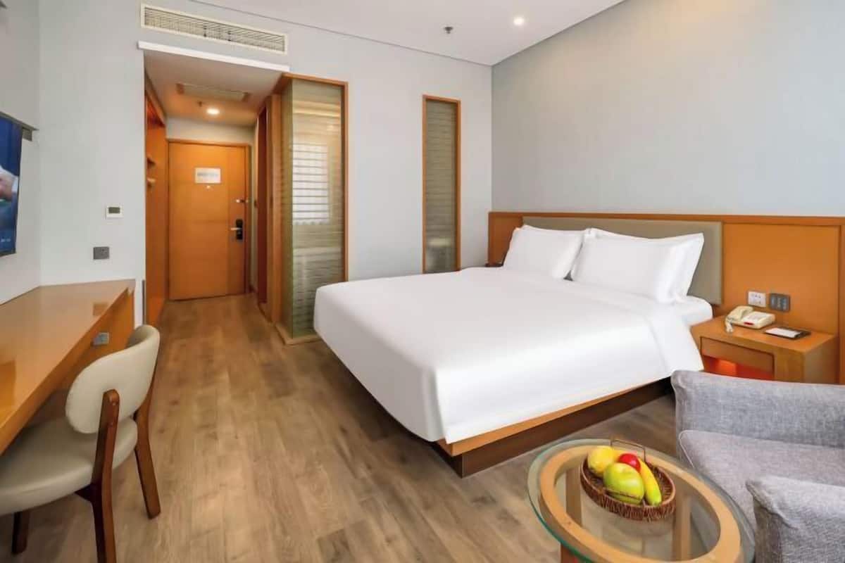 Une chambre d’hôtel avec un lit, un bureau, une chaise et une petite table sur laquelle se trouvent des fruits.