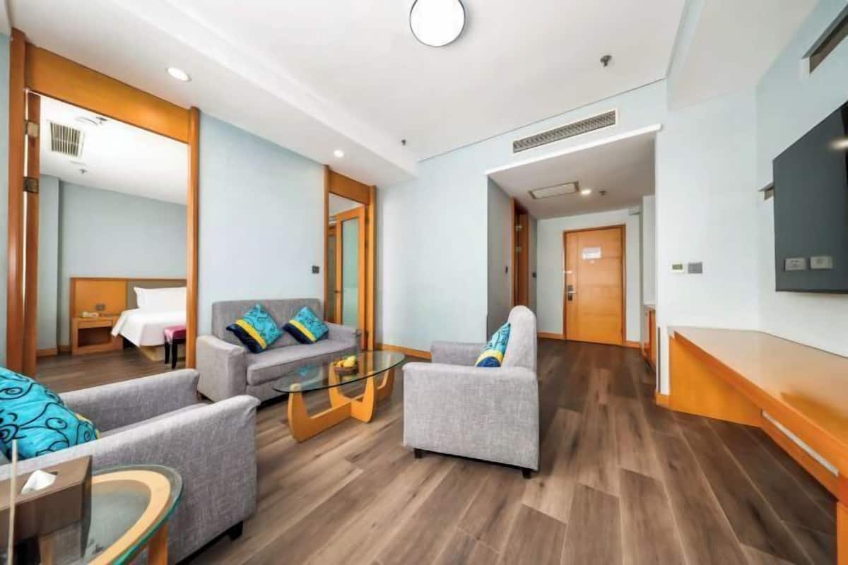 Un hall d’hôtel moderne avec un plancher en bois, des canapés gris, une table basse en verre et un téléviseur à écran plat fixé au mur.