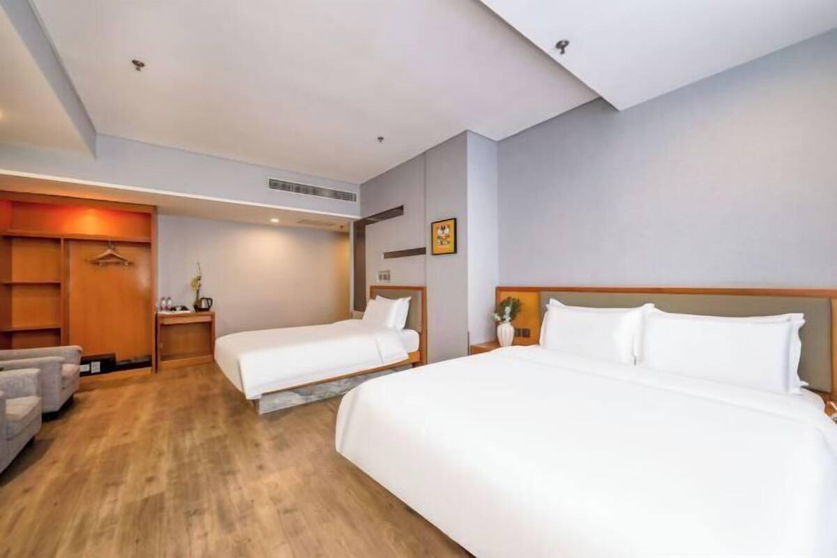 Une chambre d’hôtel avec deux lits, un canapé, une armoire et une petite table sur laquelle se trouve un vase.