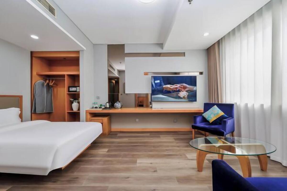 Une chambre d’hôtel équipée d’un lit, d’un bureau, d’une chaise, d’une télévision et d’une table basse en verre.