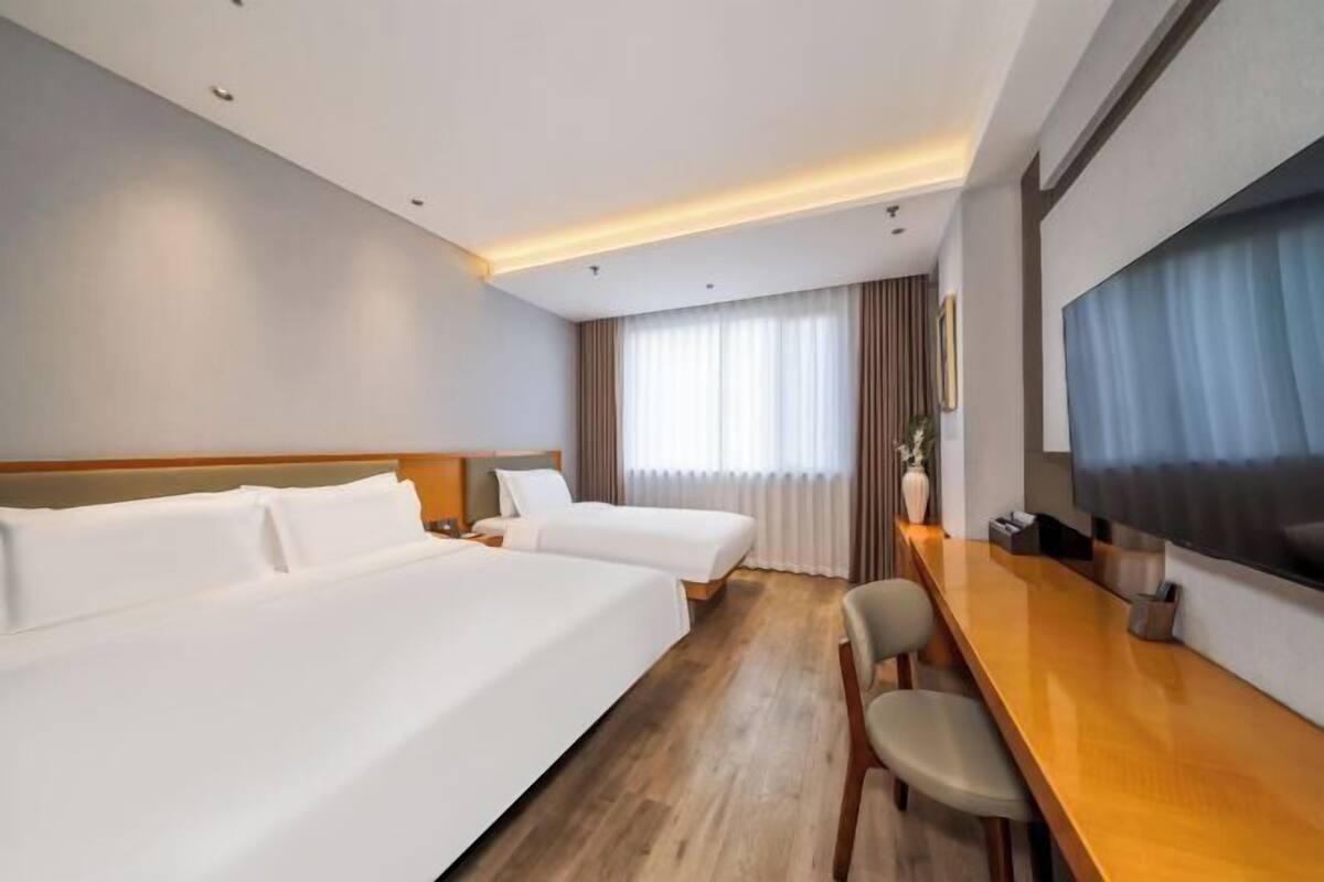 Une chambre d’hôtel avec deux lits, un bureau en bois, un téléviseur à écran plat et une grande fenêtre avec des rideaux.