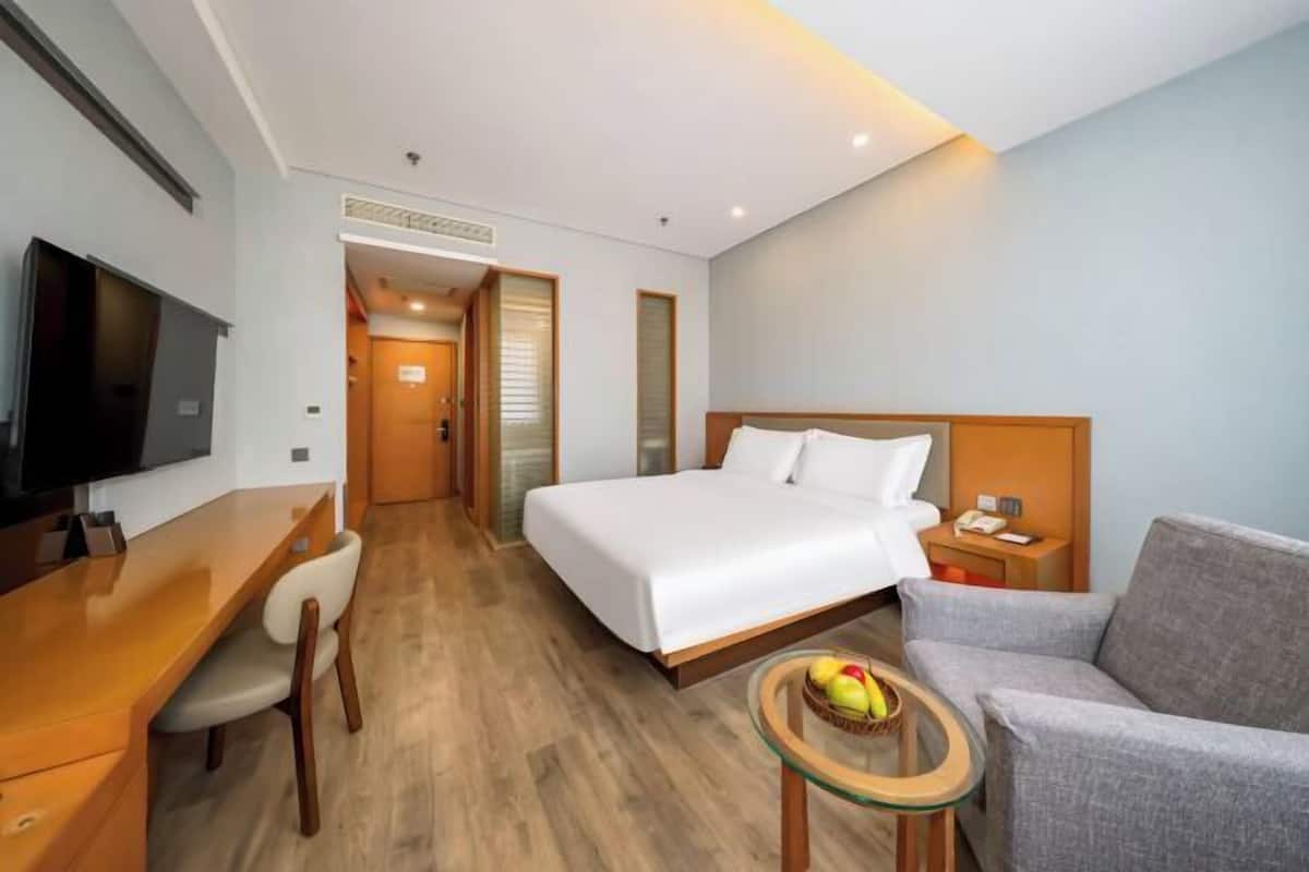 Une chambre d’hôtel avec un lit, un bureau, une chaise, une télévision et une petite table avec des fruits.
