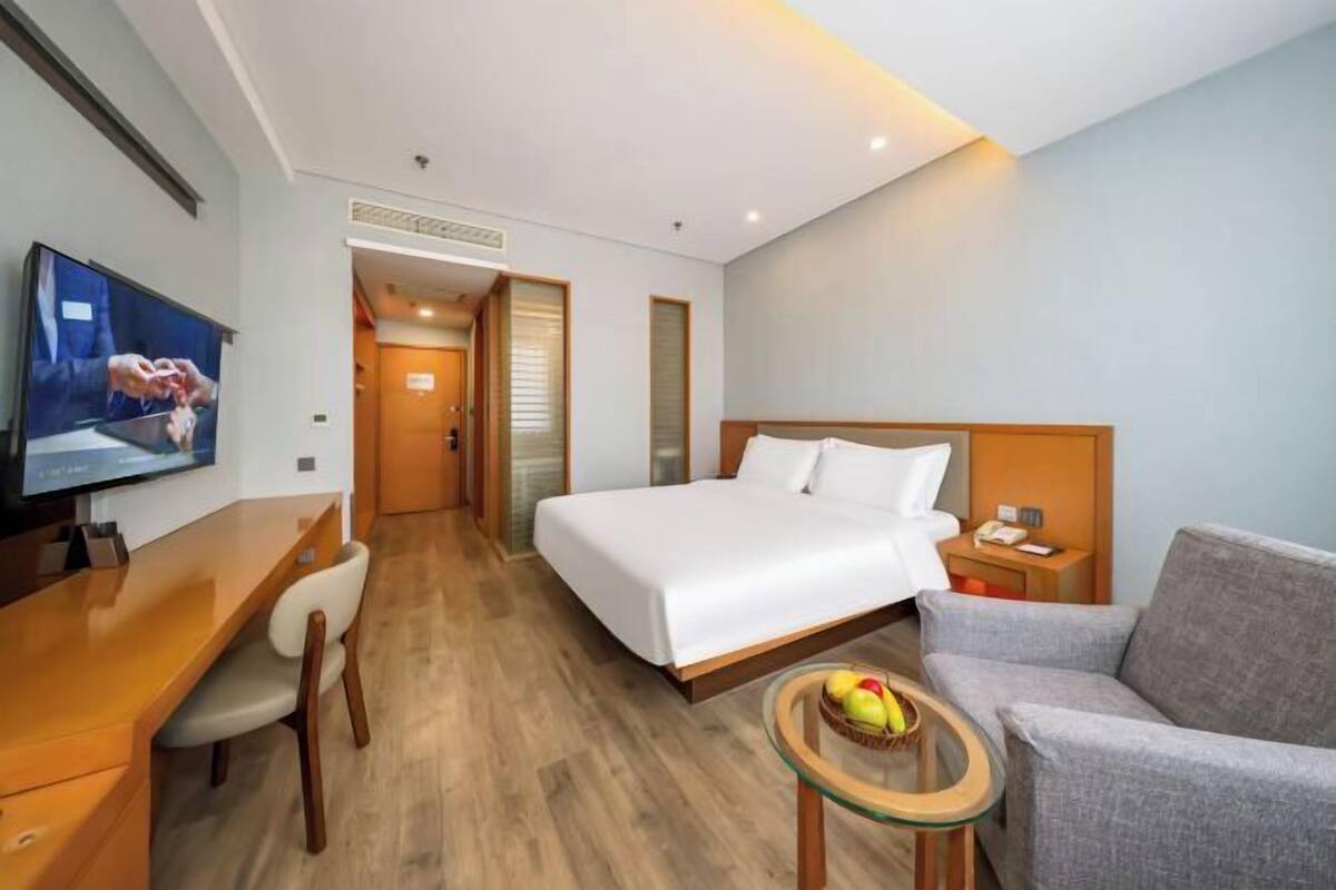 Une chambre d’hôtel avec un lit, un bureau, une télévision, une chaise et une petite table sur laquelle se trouvent des fruits.