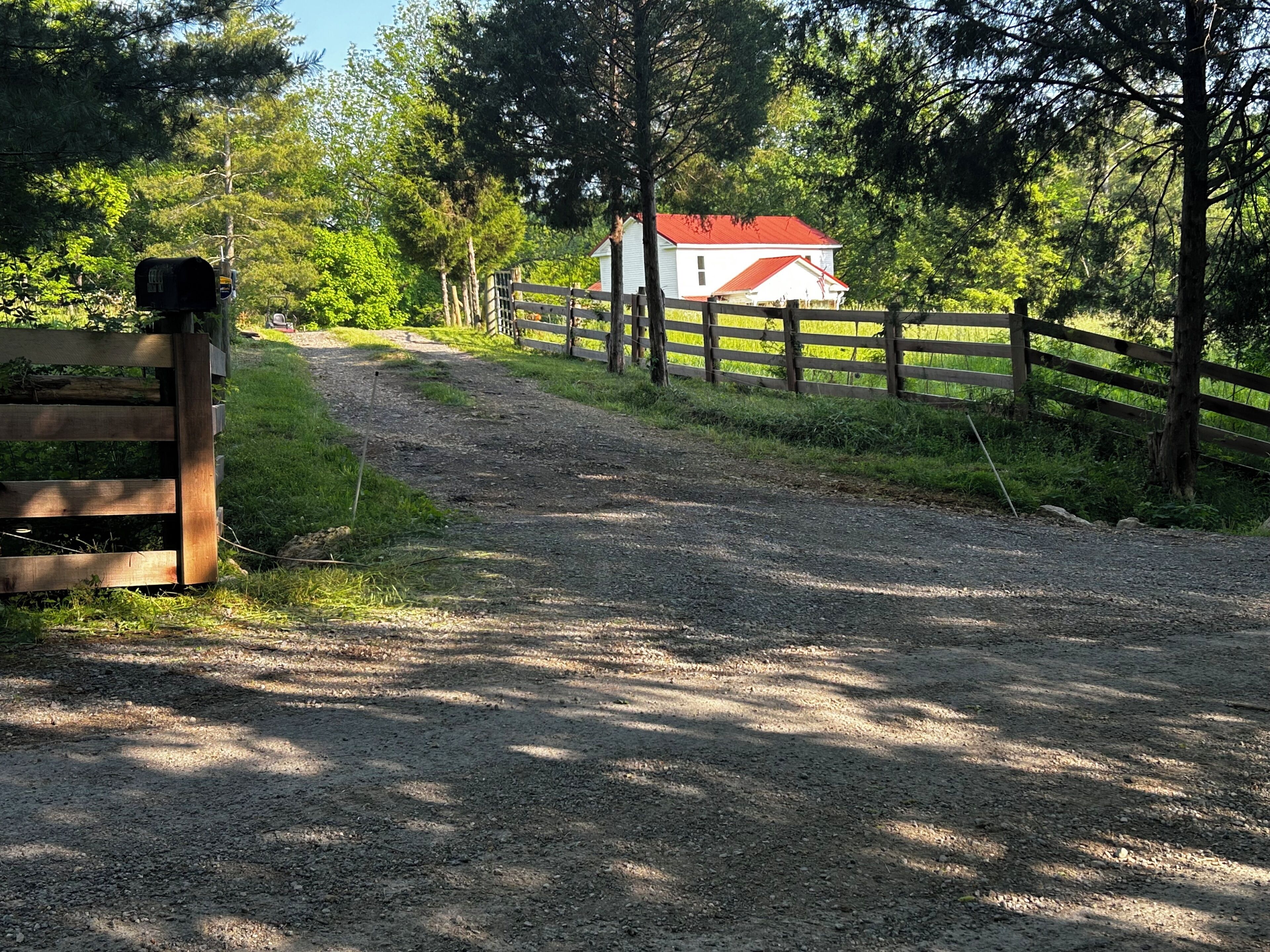A gravel path leading to a white house with a red roof, surrounded by a wooden fence and trees.