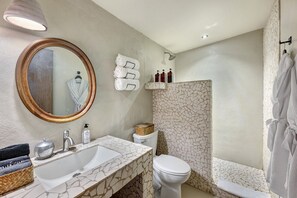 A bathroom with a stone sink, a round mirror, a toilet, a shower, and towels.