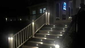 A staircase with illuminated handrails and steps, leading to a building with a visible TV screen. - Lakefront Retreat with Pool and Room For Everyone! (Milledgeville)