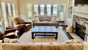 A spacious living room with a large window overlooking a body of water, a fireplace, and a comfortable seating area. - Lakefront Retreat with Pool and Room For Everyone! (Milledgeville)