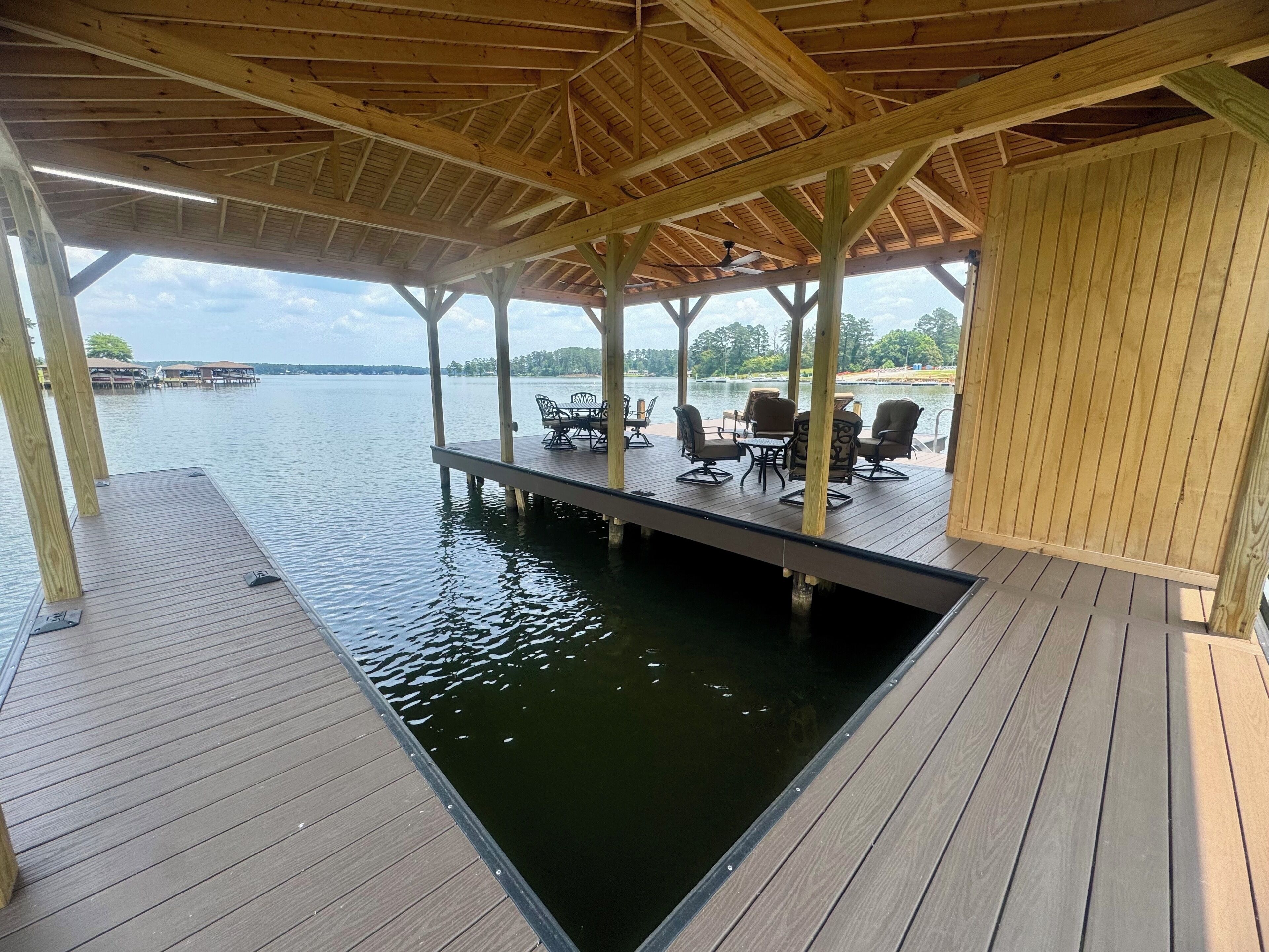 A covered wooden deck with outdoor seating and a view of a lake.