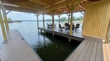 A covered wooden deck with outdoor seating and a view of a lake.