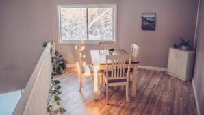 A dining area with a wooden table and chairs, a window with a view of trees, and a cabinet with a plant on top. - Spacious, newly renovated home in the forest; close to world famous fishing. (Soldotna)