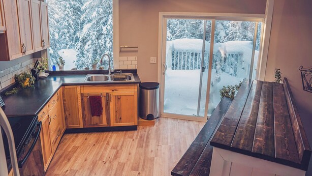 A kitchen with wooden cabinets, a sink, and a window overlooking a snowy outdoor area. - Spacious, newly renovated home in the forest; close to world famous fishing. (Soldotna)