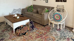 A cozy living room with a sofa, coffee table, hanging chair, and patterned rug. - Waterfront Condo with Fishing, Paddleboard, and yard access. (North Miami)