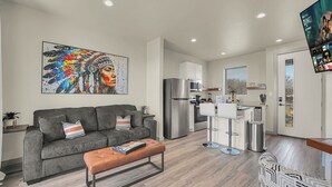 A modern living room with a grey sofa, a brown ottoman, and a colorful artwork on the wall.